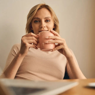 Image montrant une femme assise devant son ordinateur portable en train de boire une tasse de thé, symbolisant la détente et la productivité.