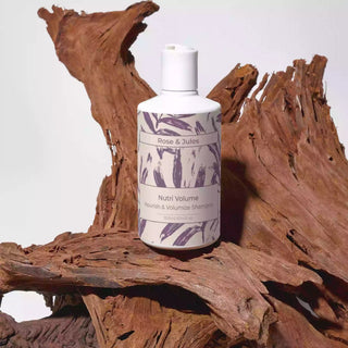 Flacon de face du shampoing "Nutri Volume" de Rose et Jules, bio, vegan et naturel, volumisateur et nourrissant, posé sur une branche de bois rouge en prise de vue studio.